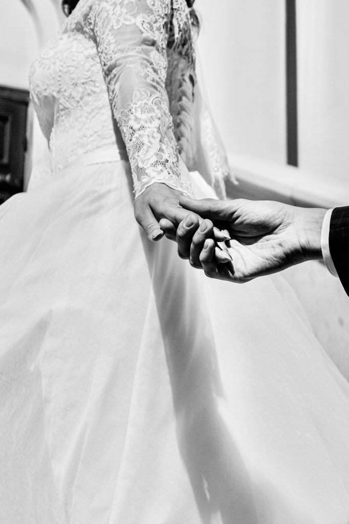 Elegancka czarno-biała fotografia uchwycająca pannę młodą trzymającą rękę swojego partnera, symbolizując miłość i zaangażowanie